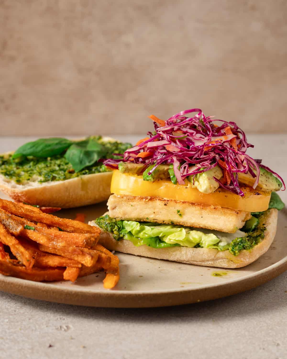 side view of crispy tofu sandwich with the top bun off on a plate.