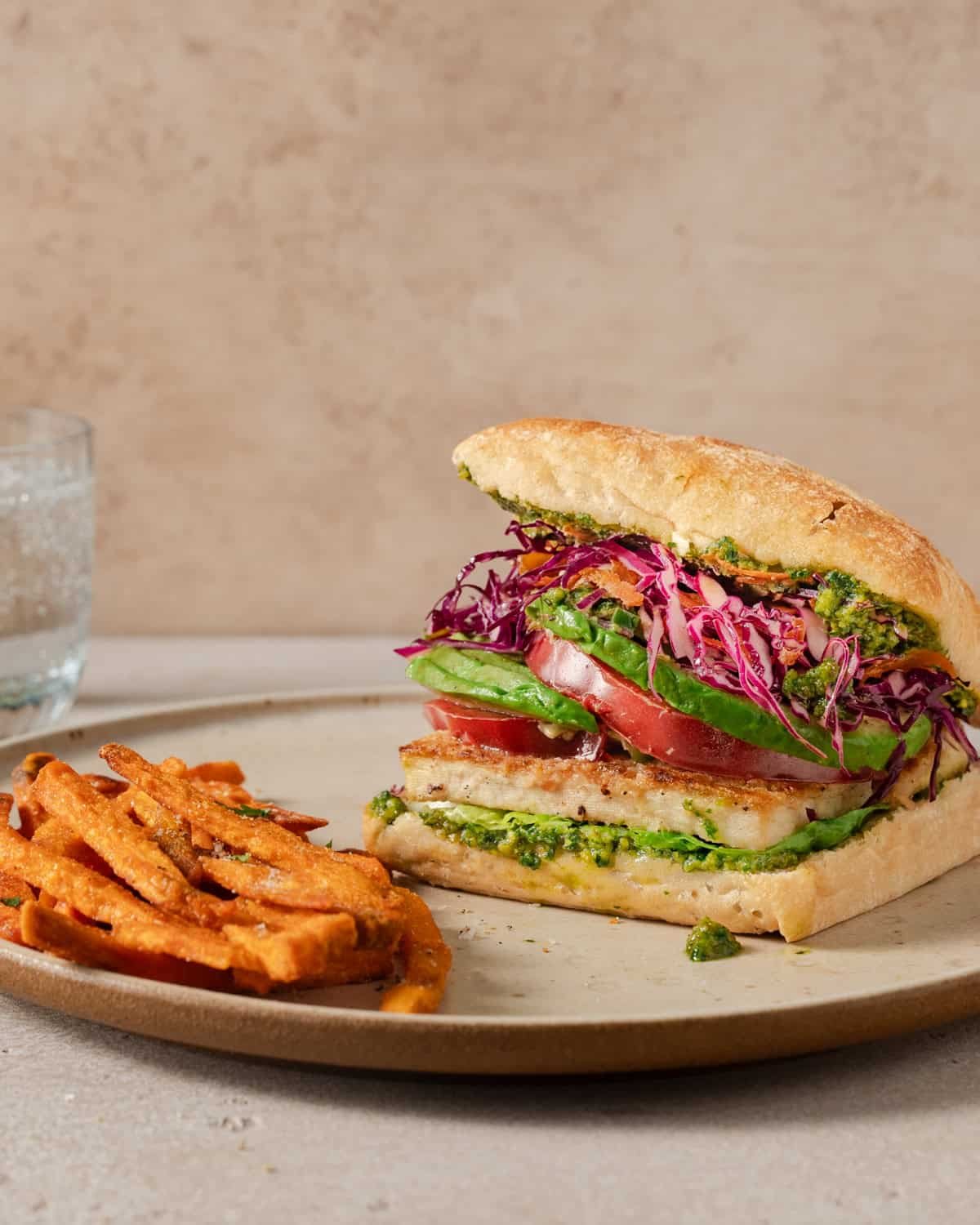 side view of crispy tofu sandwich and sweet potato fries on a plate.