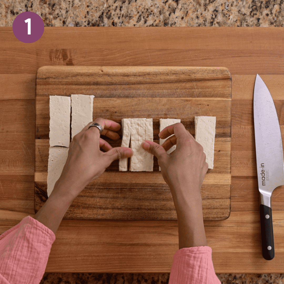 Person slicing tofu into slabs on a wooden cutting board.
