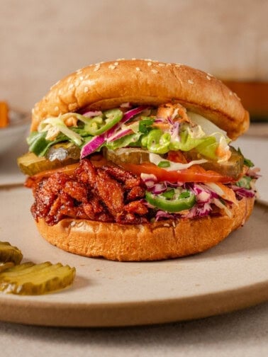 close up side view of one vegan bbq pulled pork sandwich on a plate.