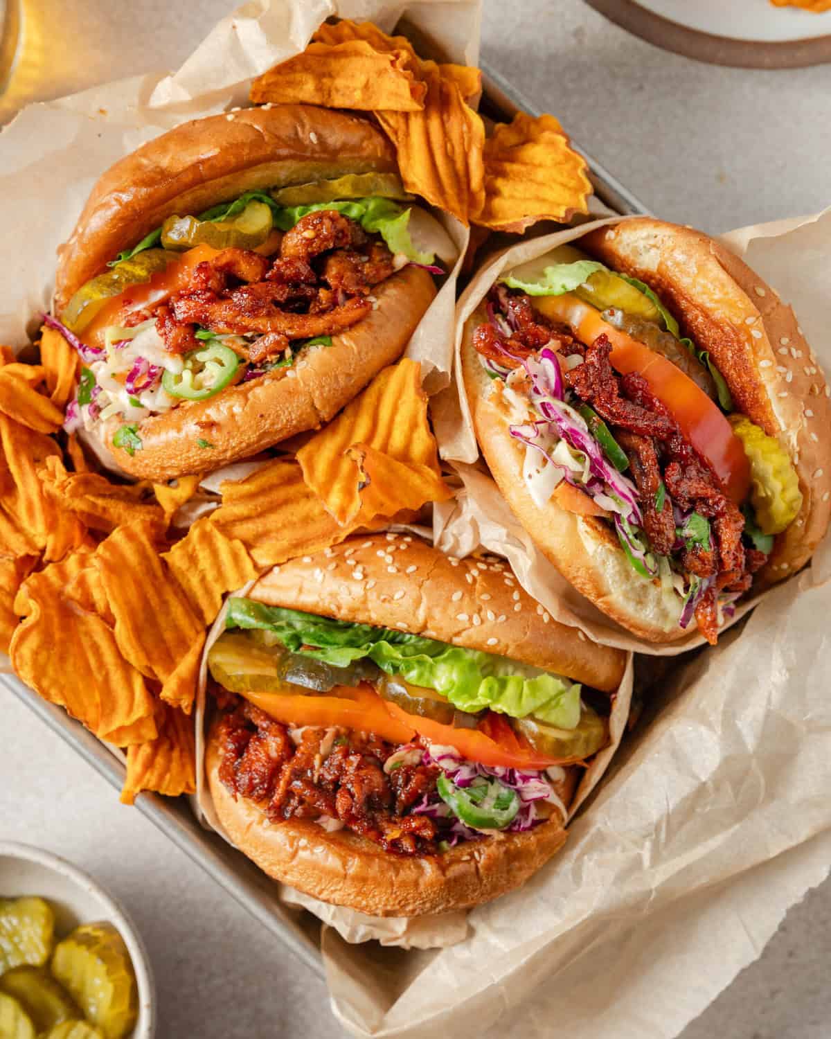 overhead view of three sandwiches facing up next to chips in a square cardboard box.