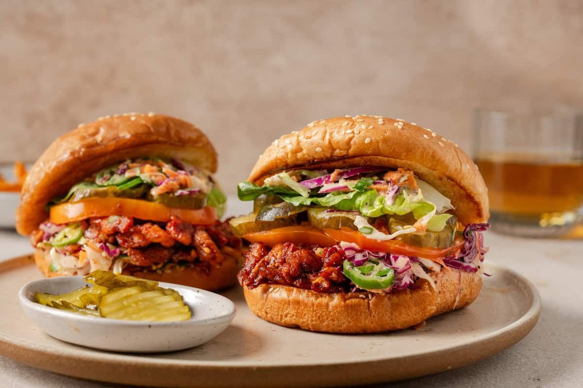 side view of two vegan pulled pork sandwiches on a plate.