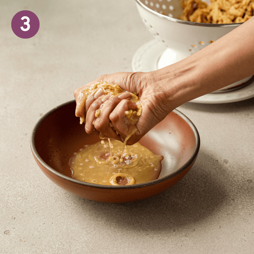 Person squeezing excess liquid out of soy curls into a bowl.