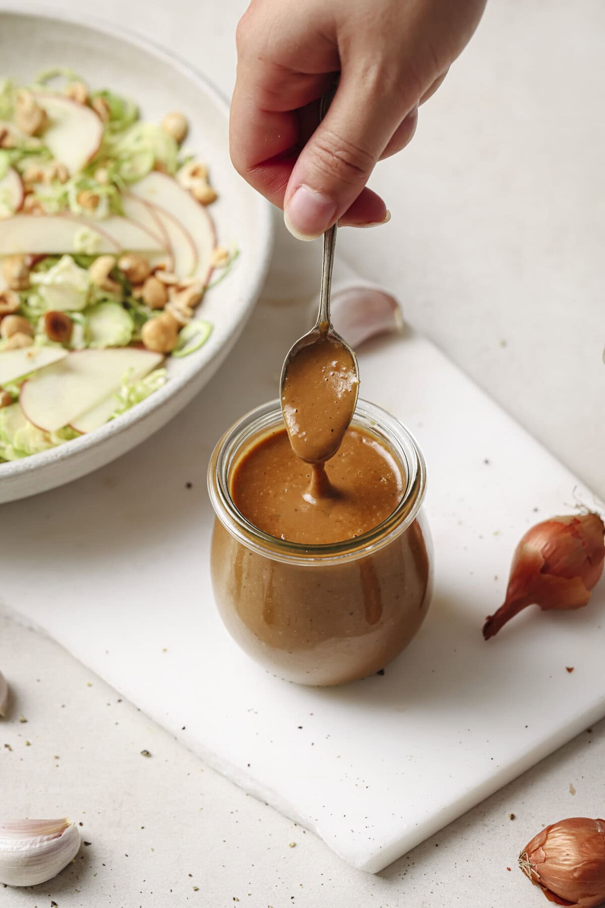 Woman's hand spooning creamy balsamic vinaigrette from a jar on a white surface.