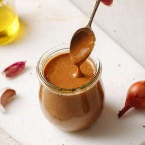 Woman's hand spooning creamy balsamic vinaigrette from a jar on a white surface.