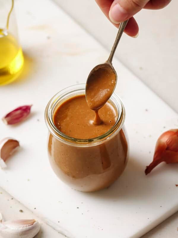 Woman's hand spooning creamy balsamic vinaigrette from a jar on a white surface.