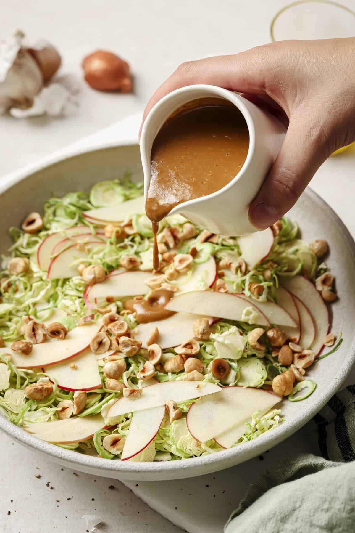 Woman's hand pouring creamy balsamic vinaigrette onto a shaved Brussels sprout salad.