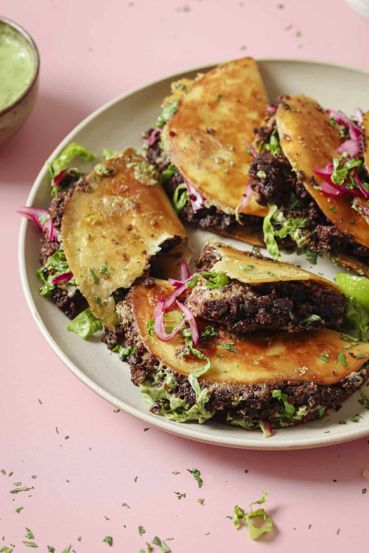 side view of a pile of crispy black bean tacos on a plate.