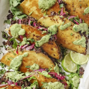 pile of black bean tacos with fillings and avocado crema on top.