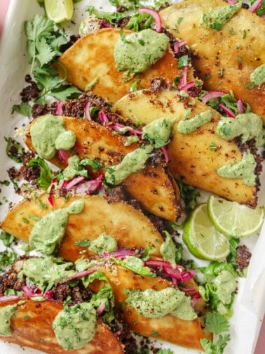 pile of black bean tacos with fillings and avocado crema on top.
