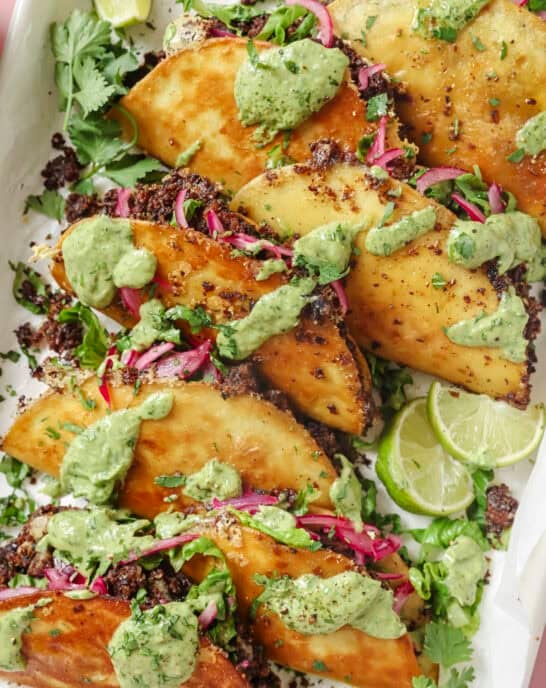 pile of black bean tacos with fillings and avocado crema on top.
