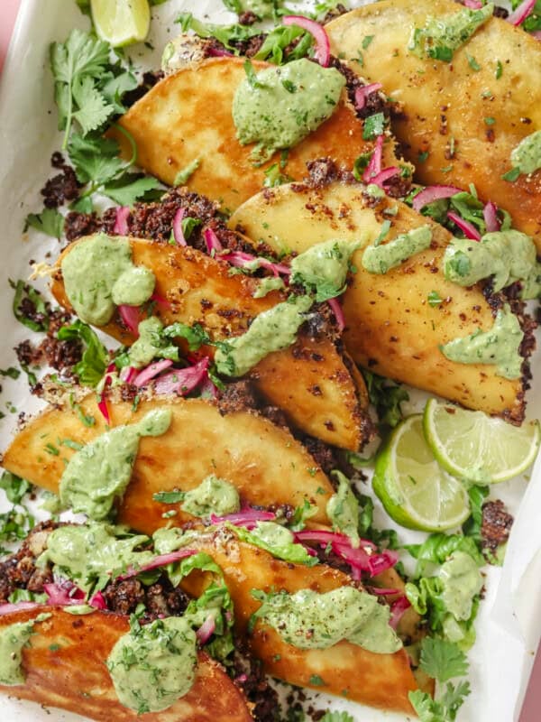 pile of black bean tacos with fillings and avocado crema on top.