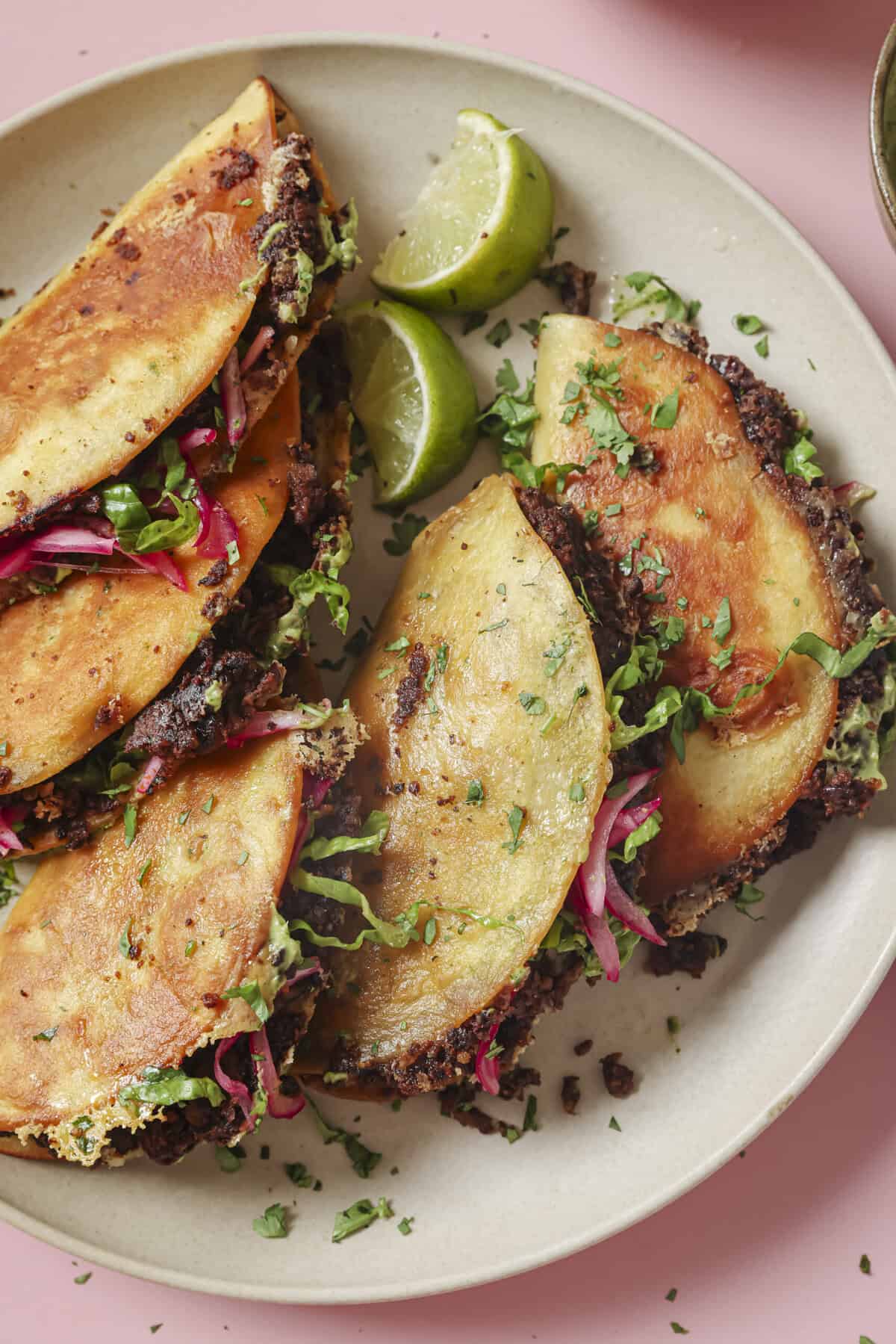 close up of 5 crispy black bean tacos on a plate with cilantro and a lime wedge.