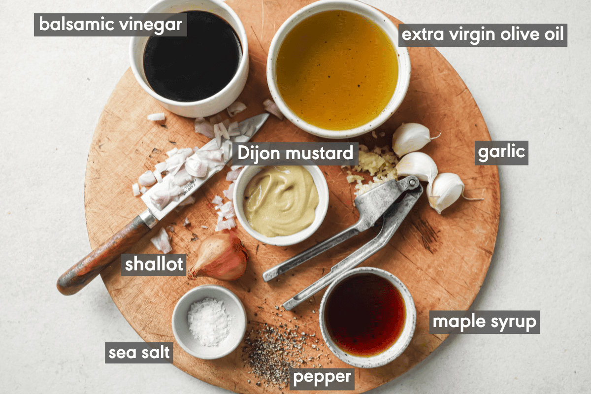 ingredients for balsamic vinaigrette in small bowls on a wooden cutting board.
