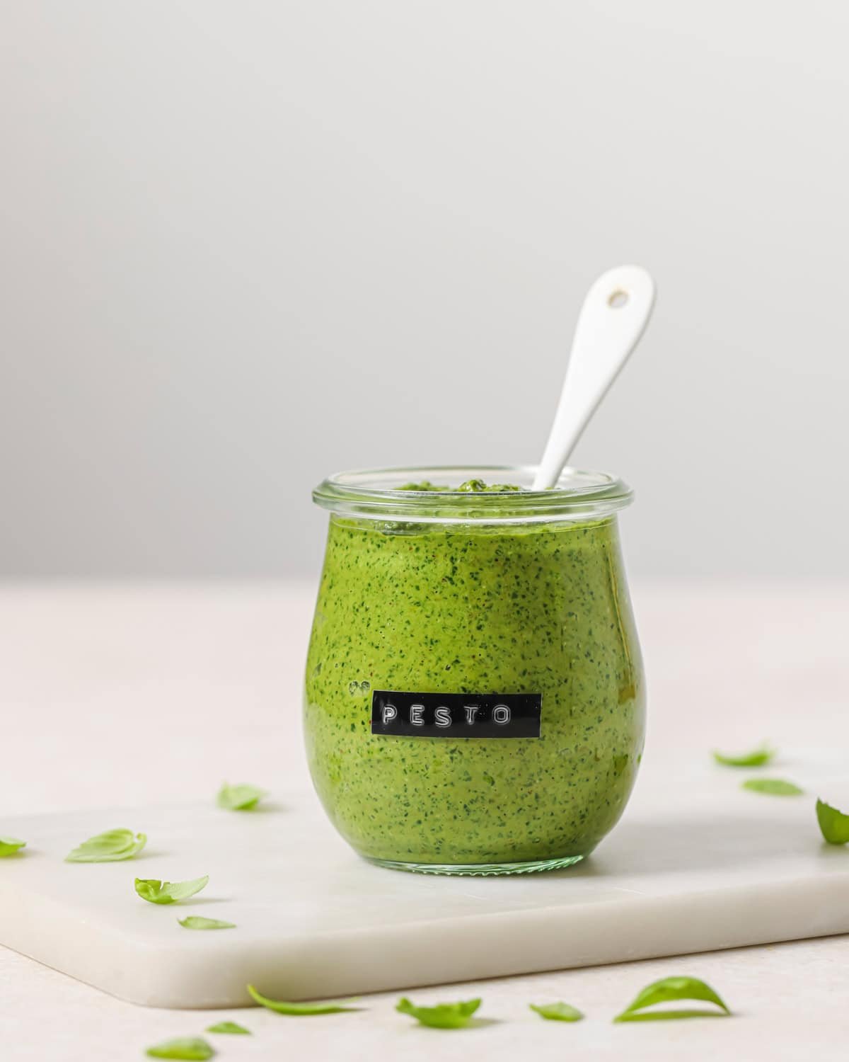 small jar of pesto with a spoon in it sitting on a white marble serving board.