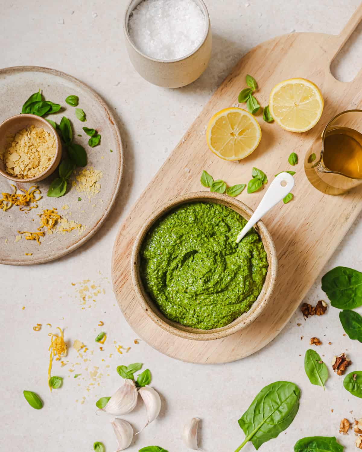 Counter with ingredients for making pesto and a bowl of pesto with a spoon in it.