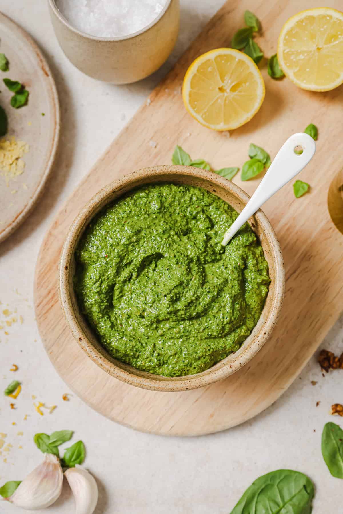 small bowl of pesto with a spoon in it sitting on a wooden serving board.