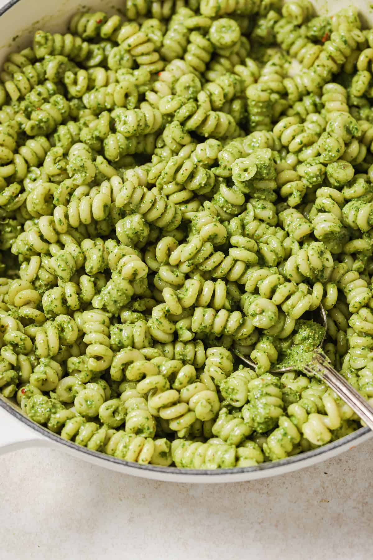 close up of spiral pesto pasta in a large pot with a spoon iin it.