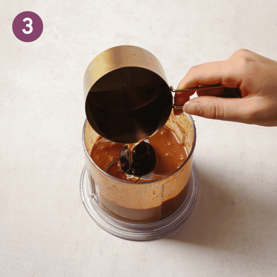 person pouring oil into small food processor.