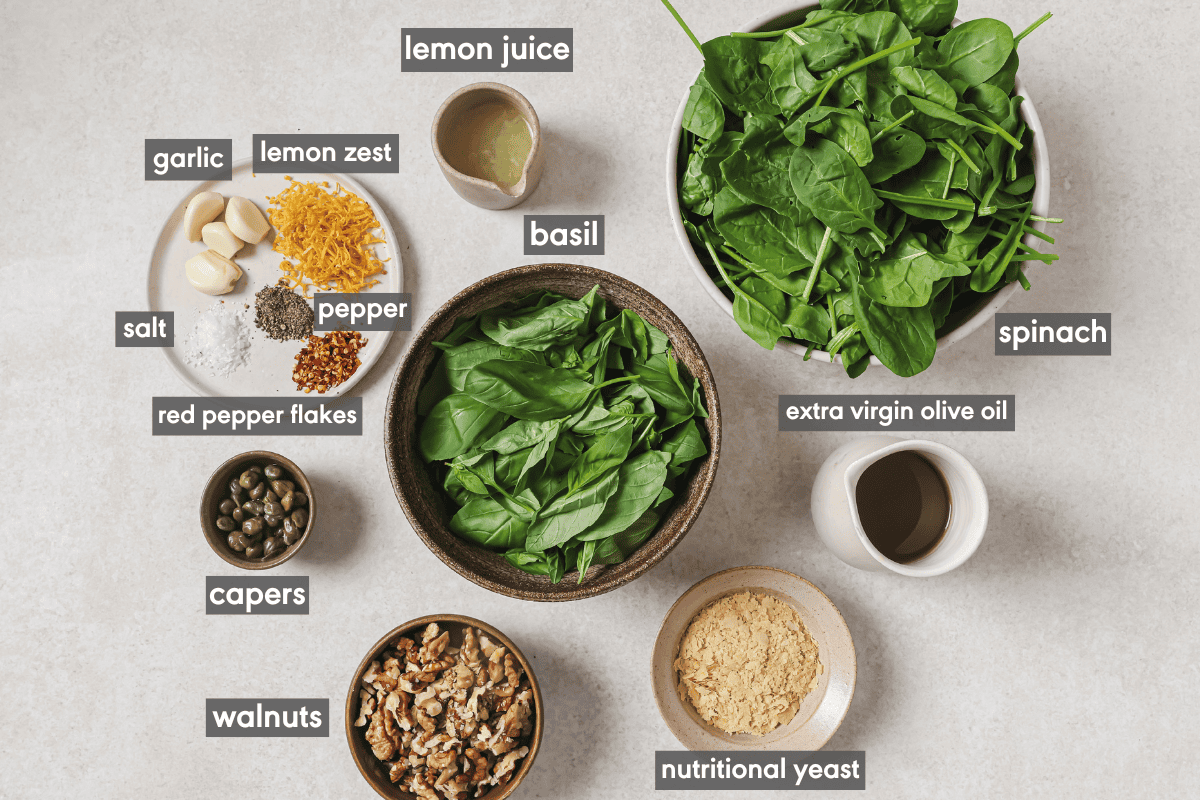 ingredients for spinach pesto in various bowls on a table.