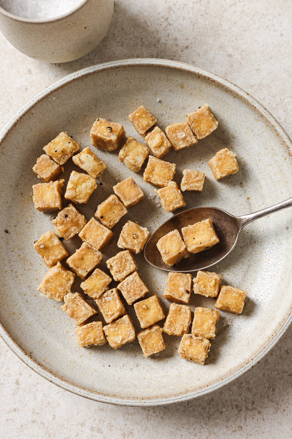 person scooping up two cooked tofu cubes from a bowl.