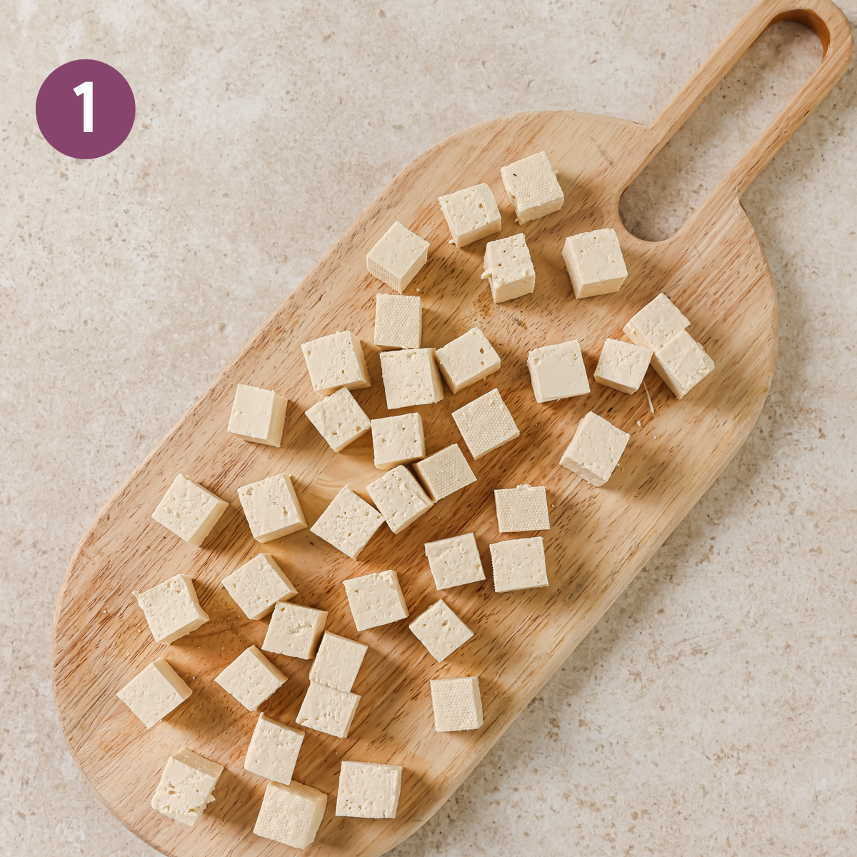 raw tofu cubes on a wooden cutting board.