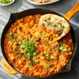 Curry topped with cilantro and serrano slices, served in a skillet with naan.