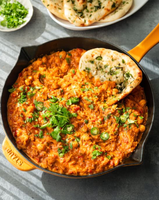 Curry topped with cilantro and serrano slices, served in a skillet with naan.