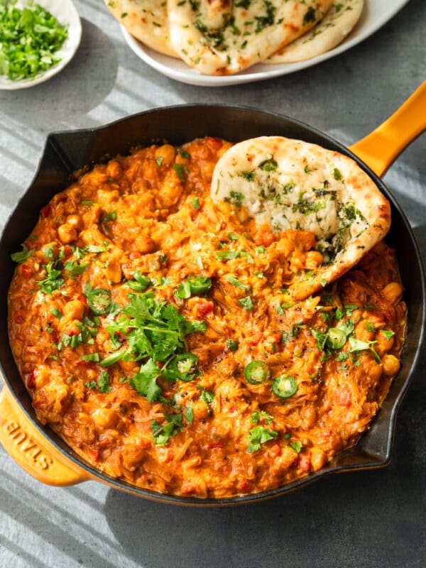 Curry topped with cilantro and serrano slices, served in a skillet with naan.