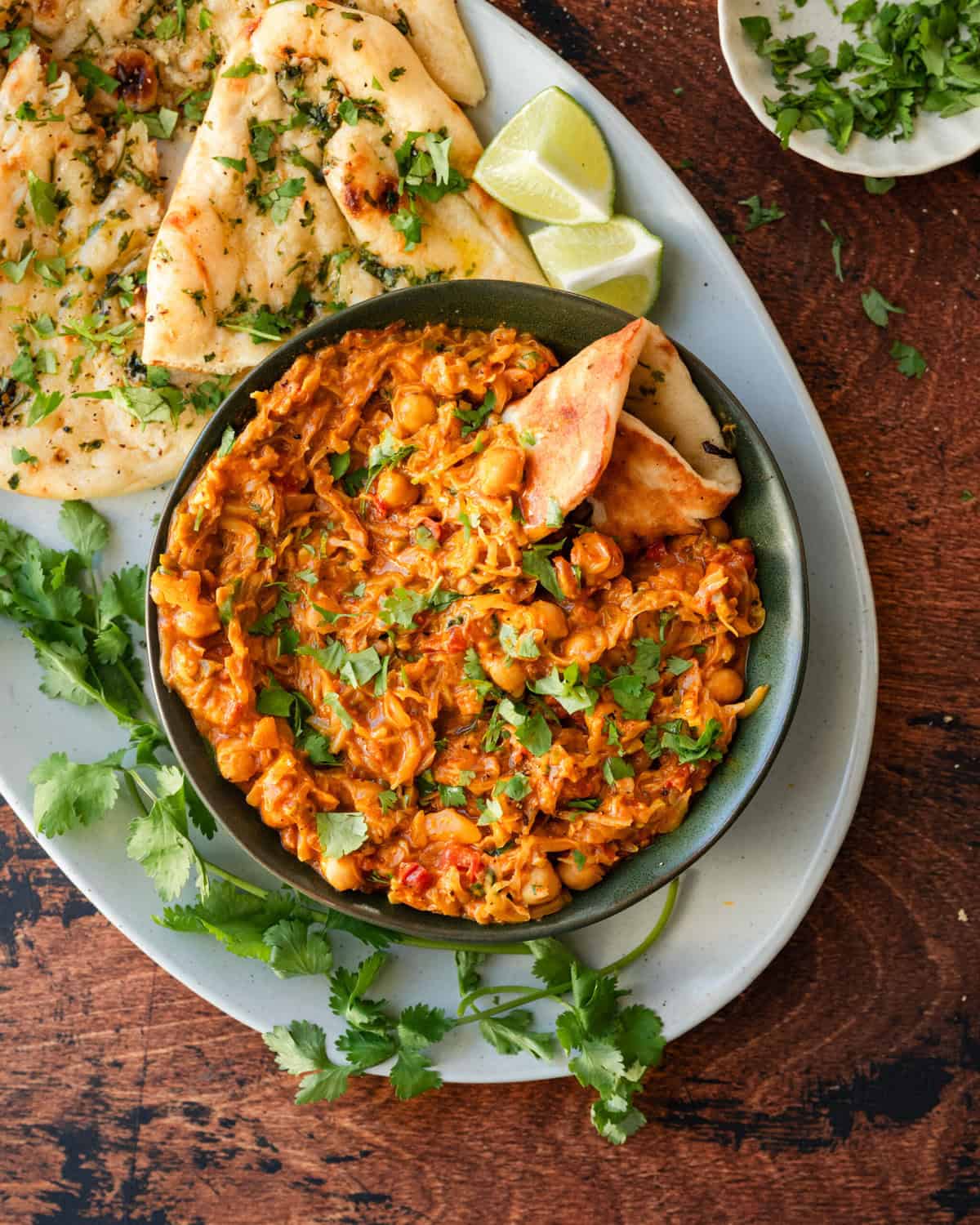 bowl of cabbage curry on platter next to garlic naan.