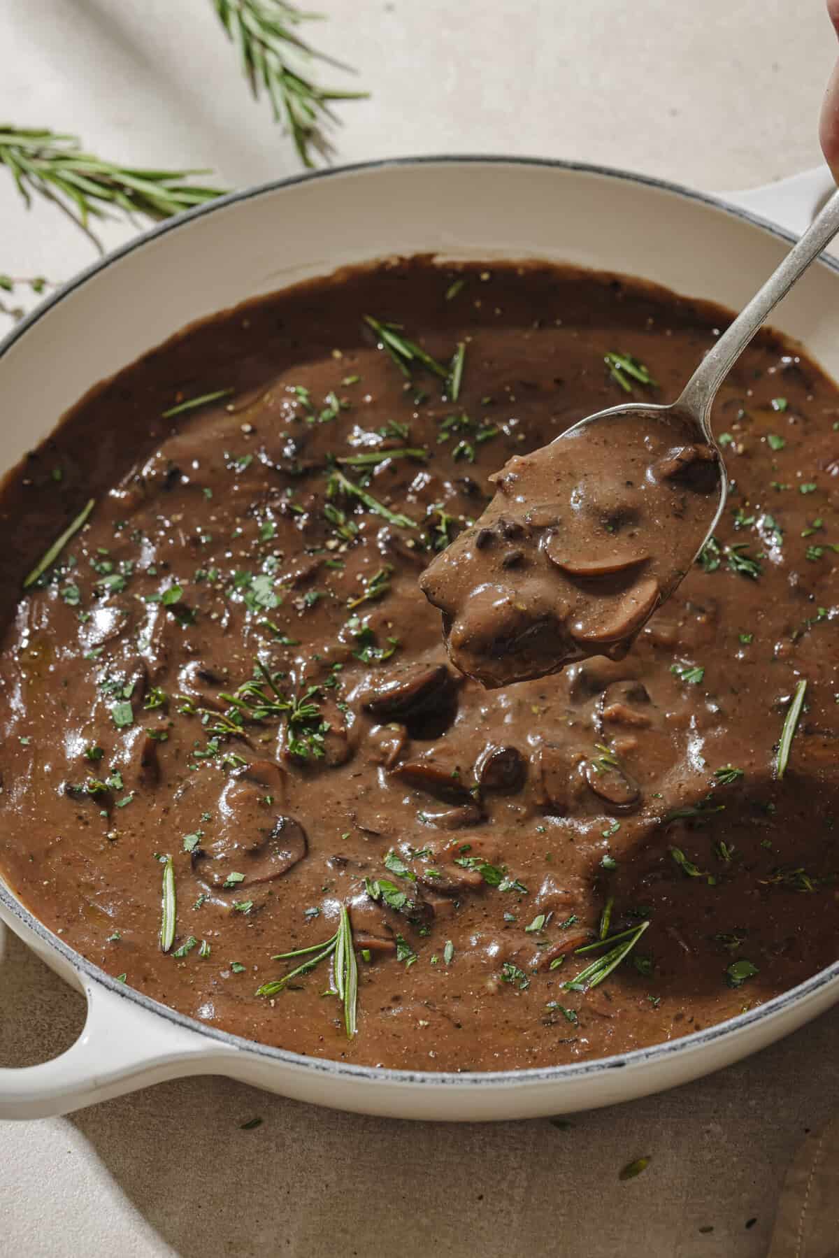 Gravy with herbs and a spoon in a frying pan.