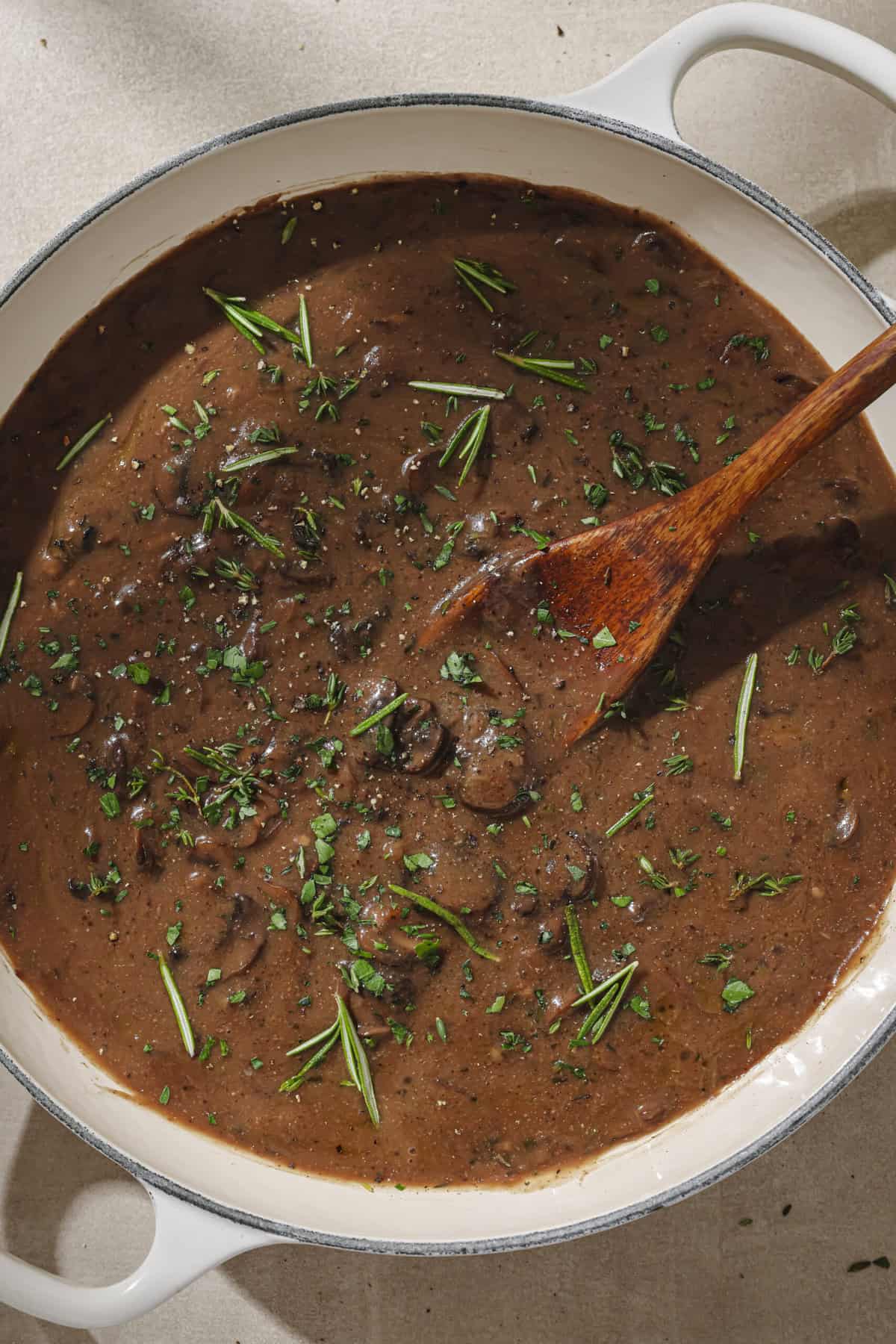 Gravy with herbs and a wooden spoon in a frying pan.