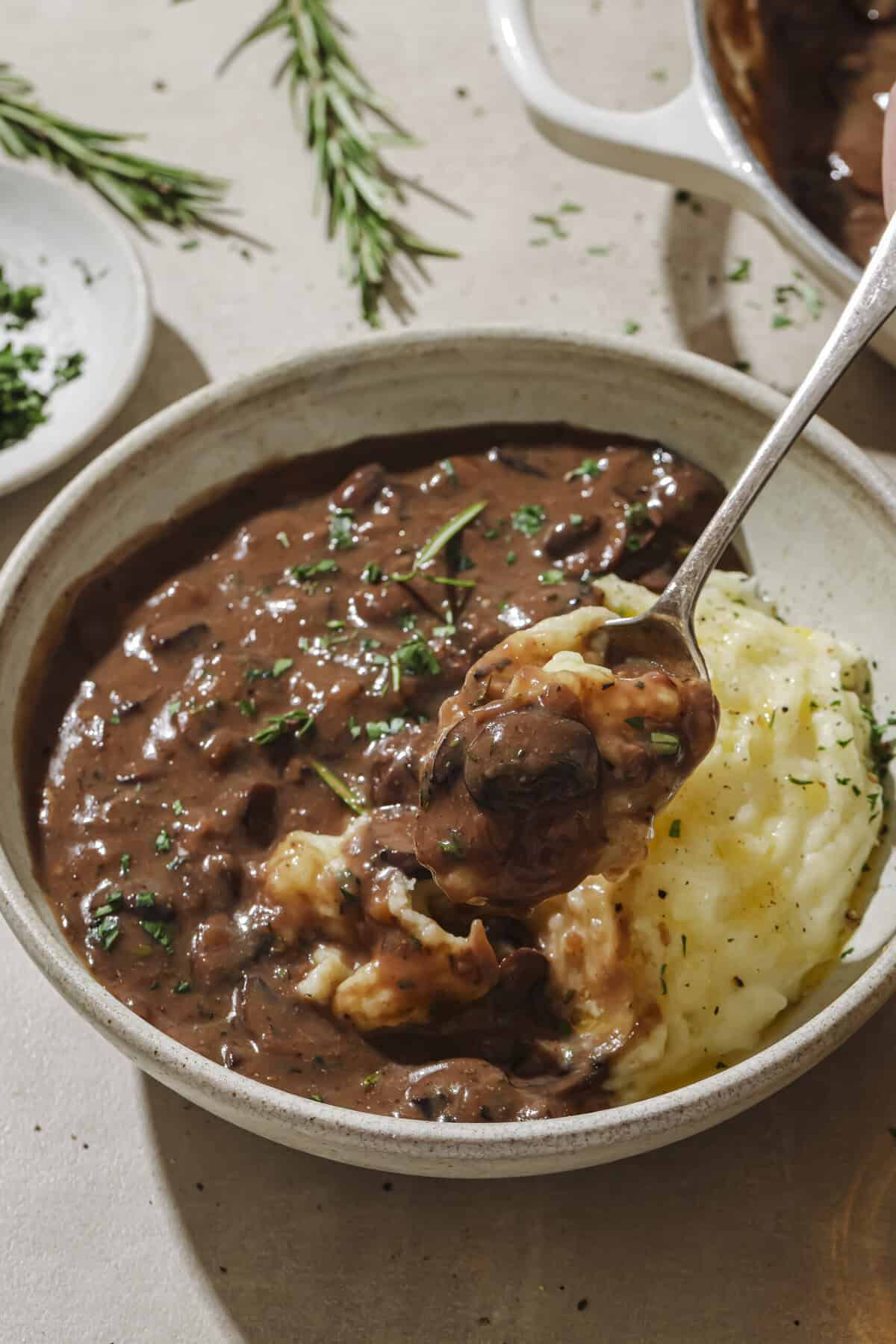Person taking a spoonful of mashed potatoes and gravy from a bowl.