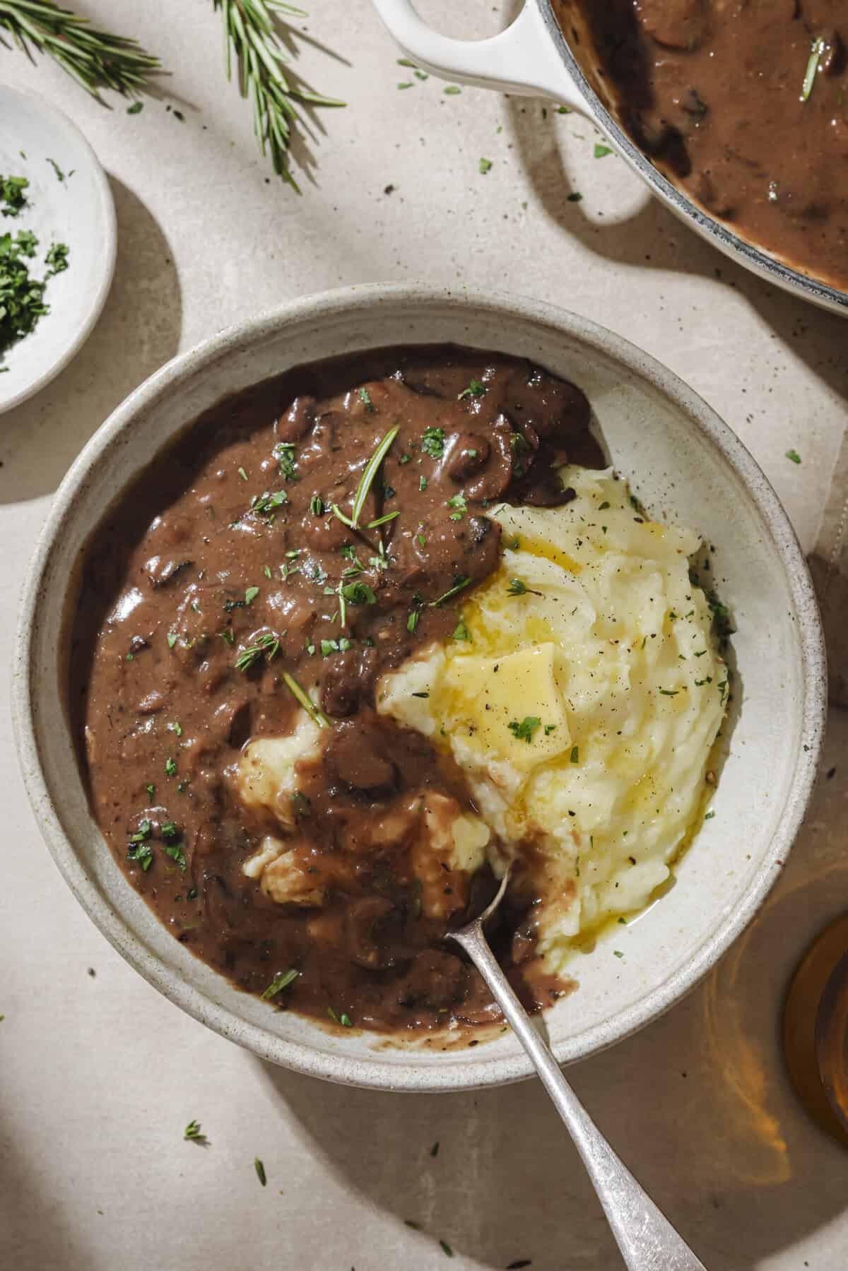 overhead view of a metal spoon inside of vegan mashed potatoes and gravy in a bowl.
