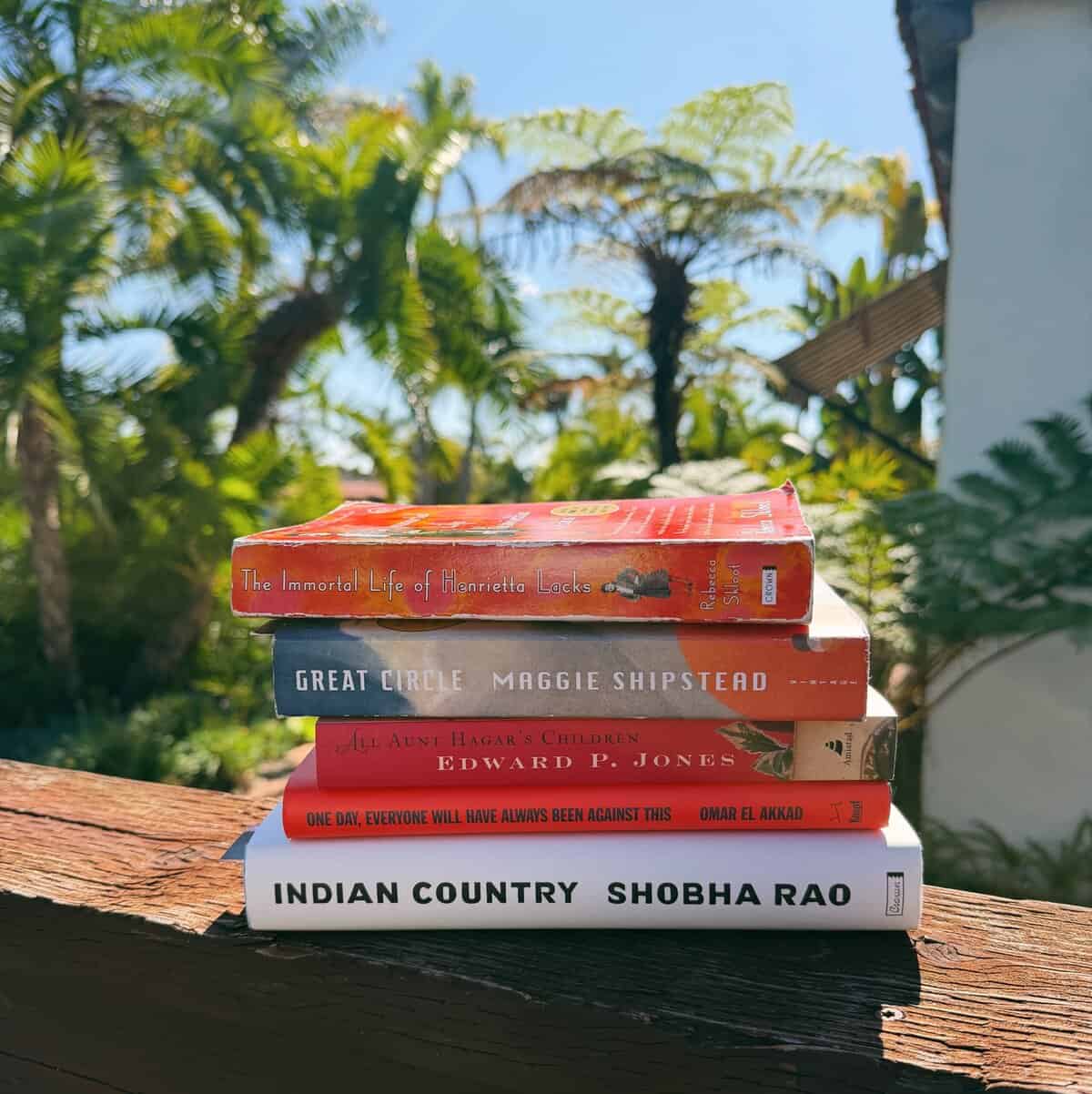 a stack of five books on a ledge in front of palm trees.