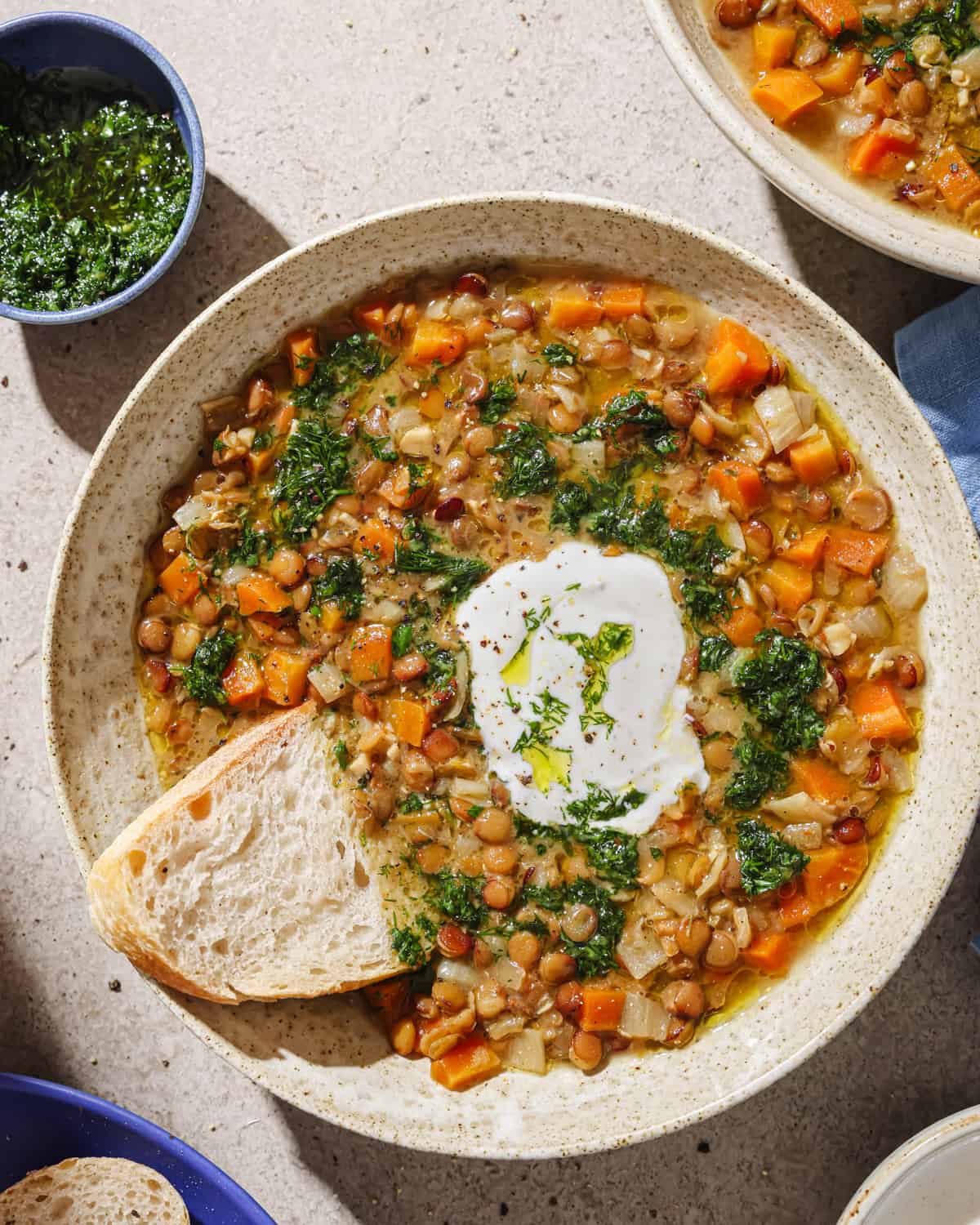 overhead view of lentil soup in a bowl next to small bowl of herby oil.