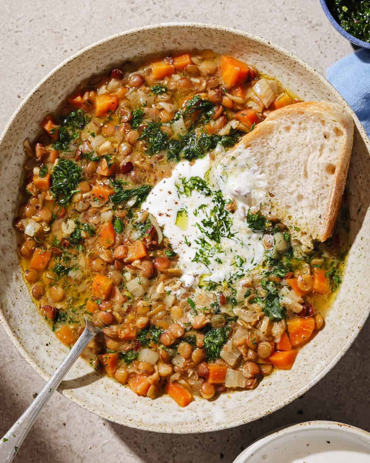 Lentil soup with carrots in a bowl garnished with herbs, yogurt sauce, and bread.