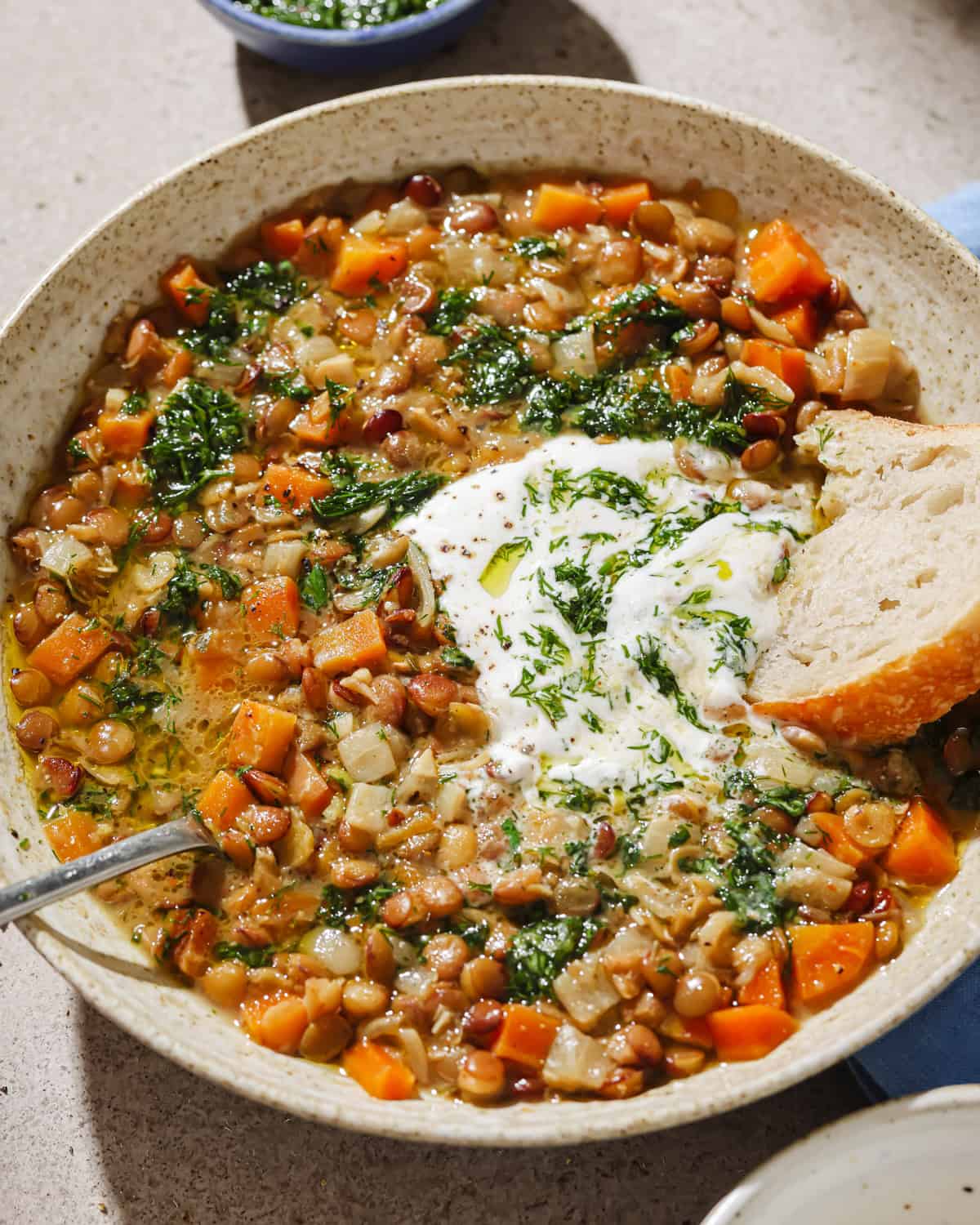 backlit angled photo of lentil soup in a bowl next to small bowl of herby oil.