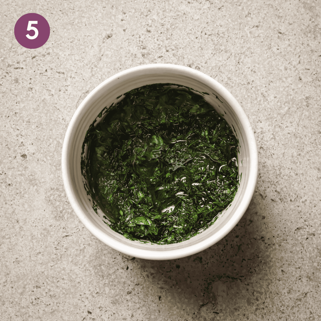 finely chopped fresh herbs with olive oil in a white bowl.