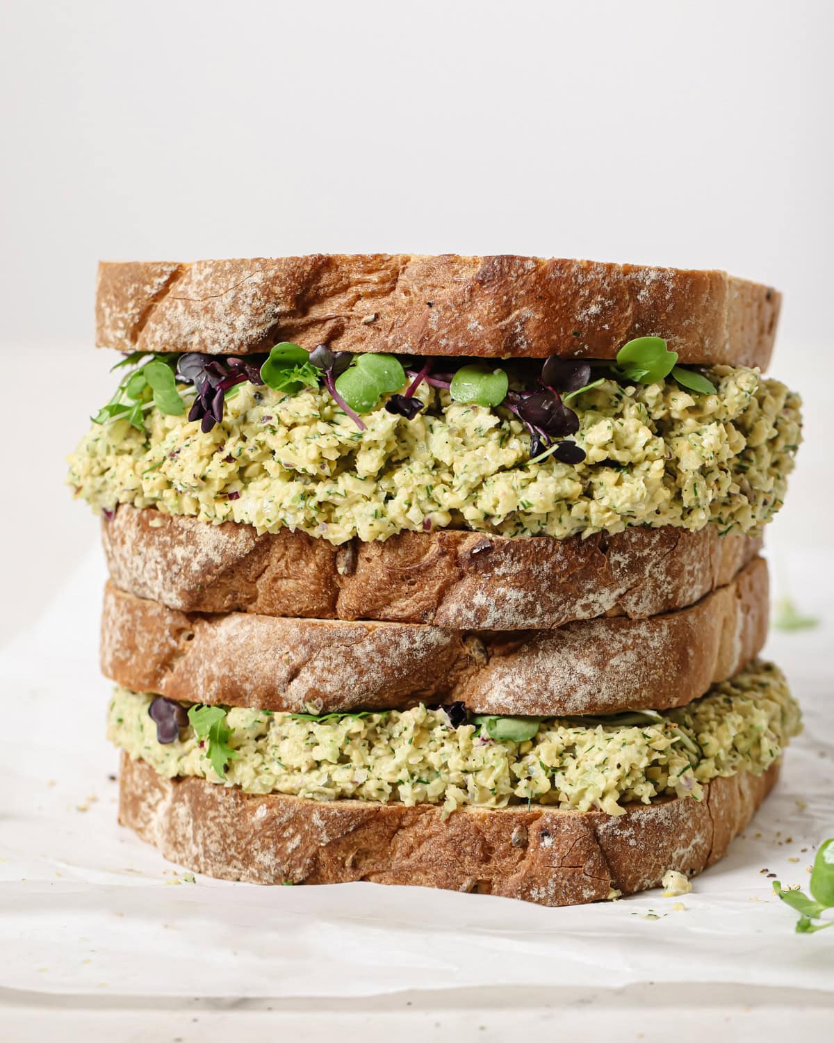 two full chickpea salad sandwiches stacked on top of one another on a piece of parchment paper.