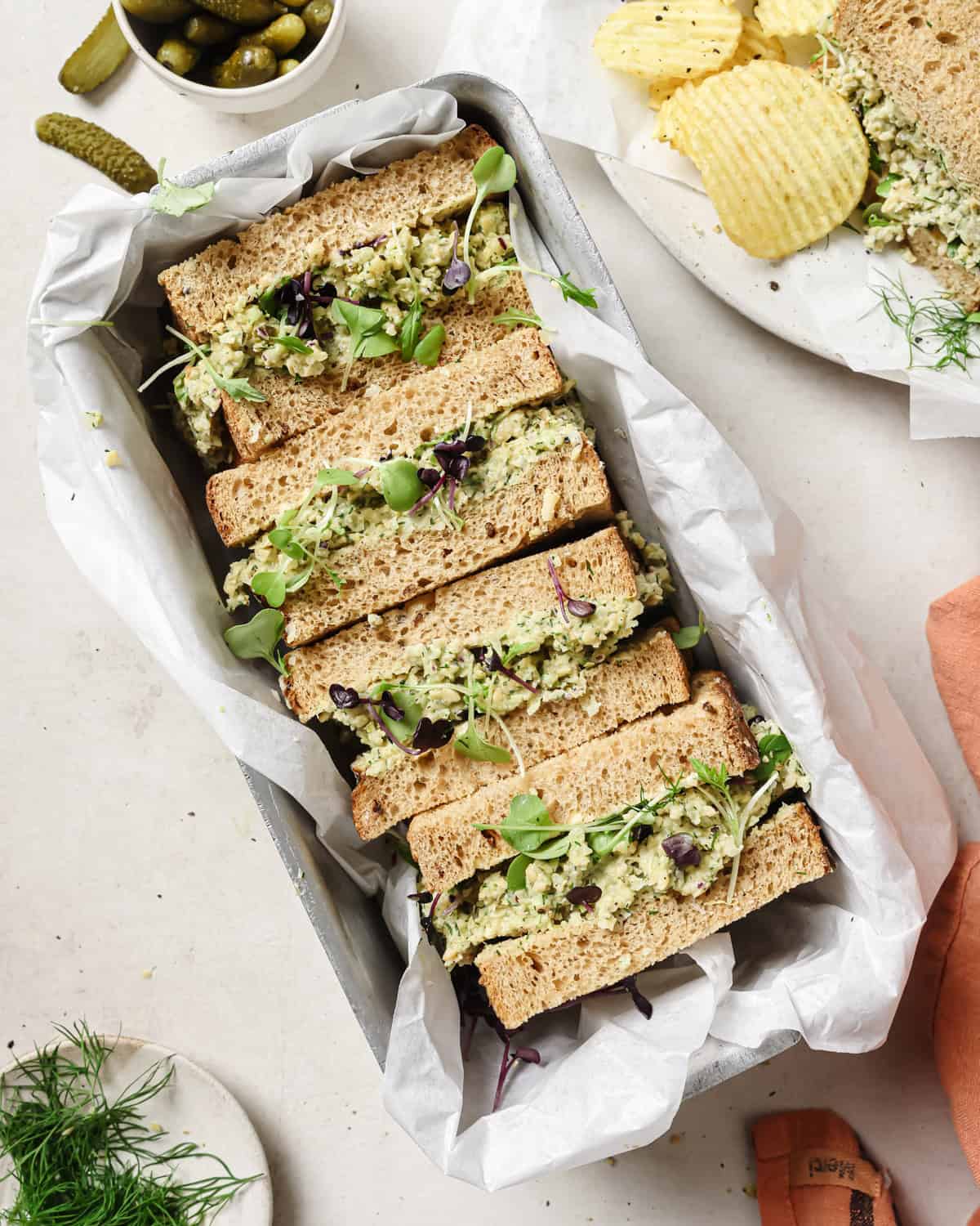 four chickpea salad sandwich halves in a loaf pan lined with parchment paper.