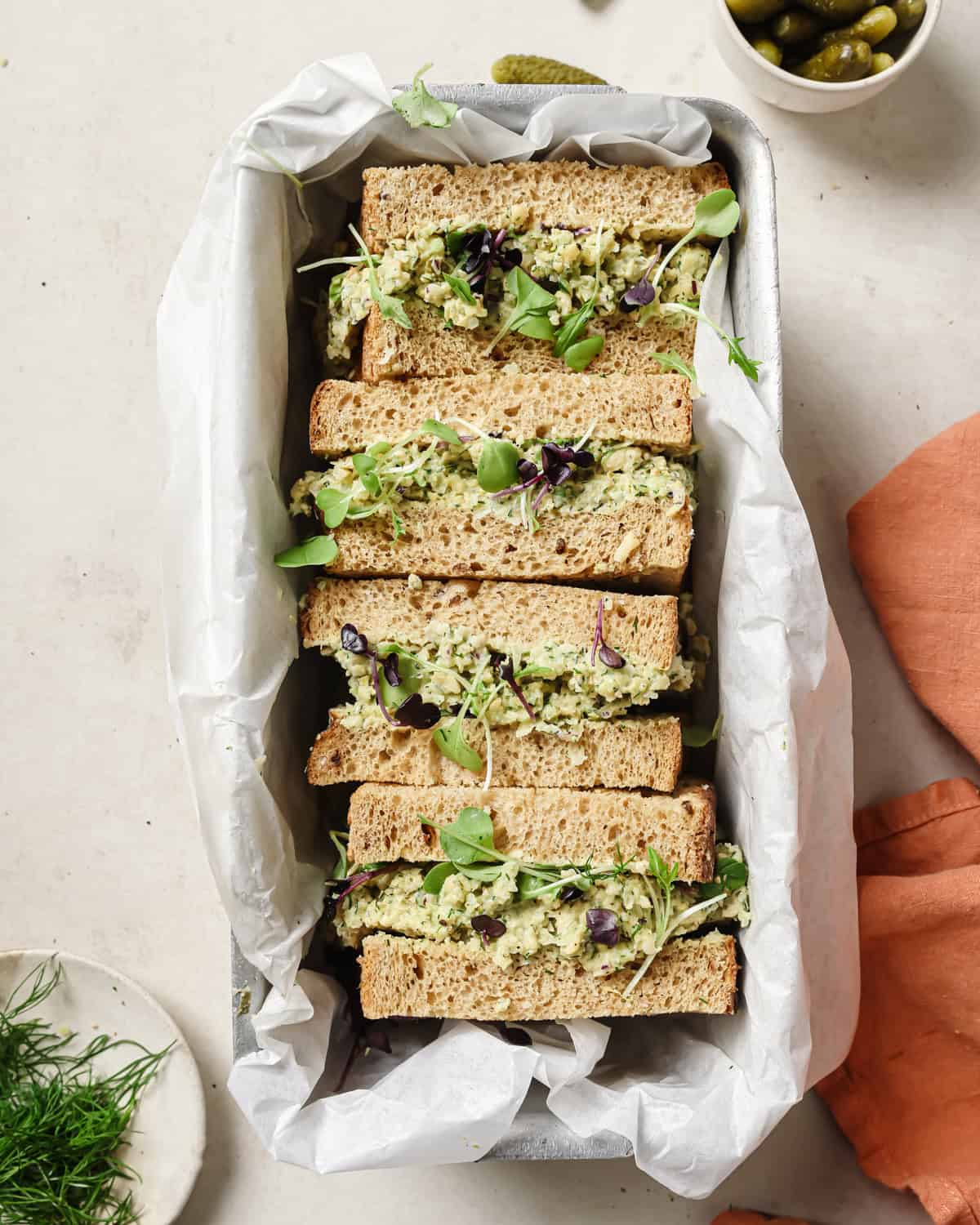 four chickpea salad sandwich halves in a loaf pan lined with parchment paper.