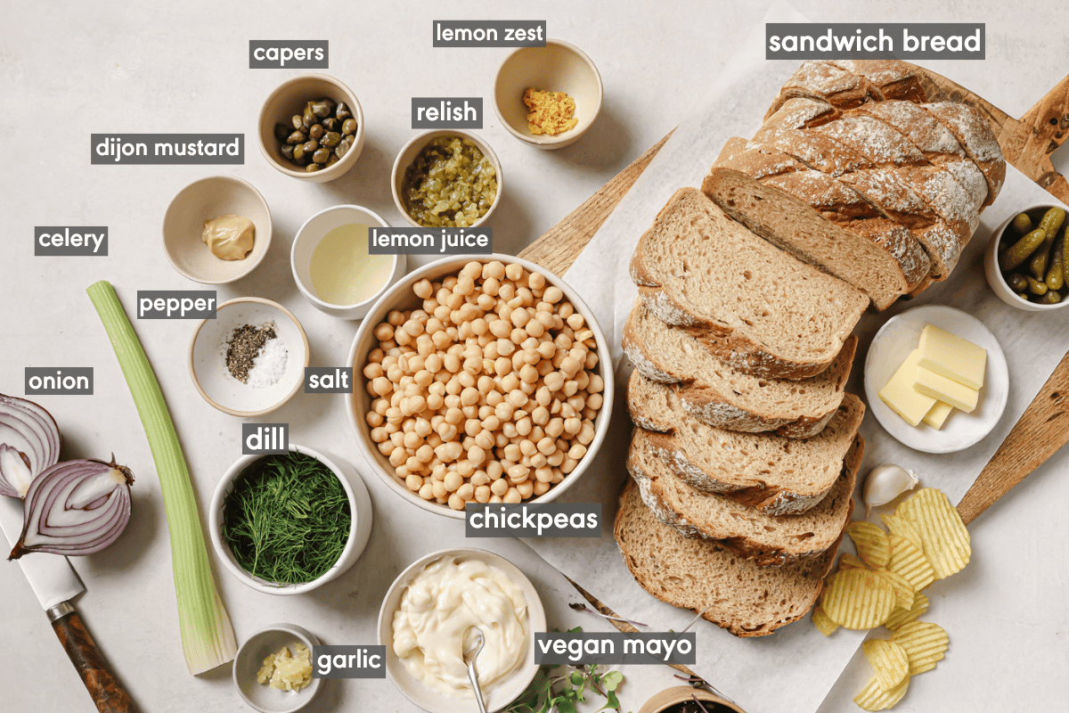 chickpea salad sandwich ingredients laid out on a cutting board and in various bowls on a table.