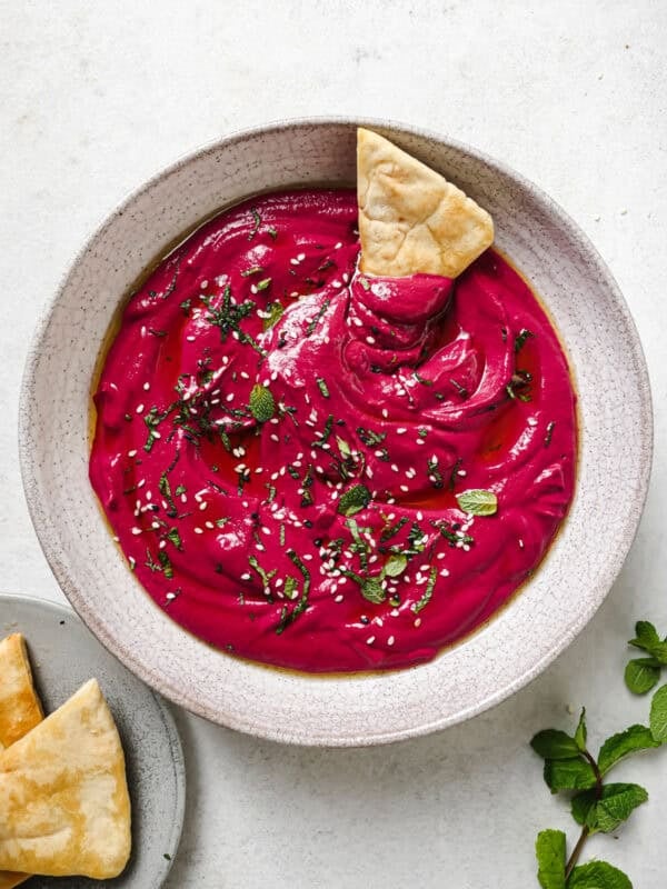 Overhead shot of silky beet dip with sesame seeds, mint, and pita bread.