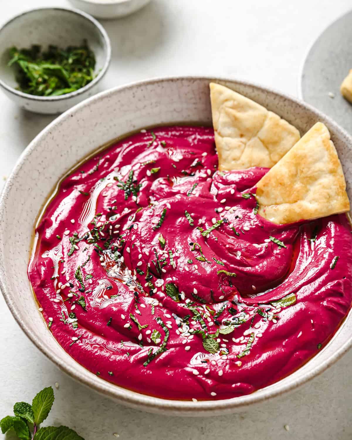 Overhead shot of beet dip with sesame seeds, mint, and pita bread next to a small bowl of chopped mint.