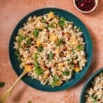 Bowl of herbed rice salad on a table next to a small bowl of pomegranate seeds.