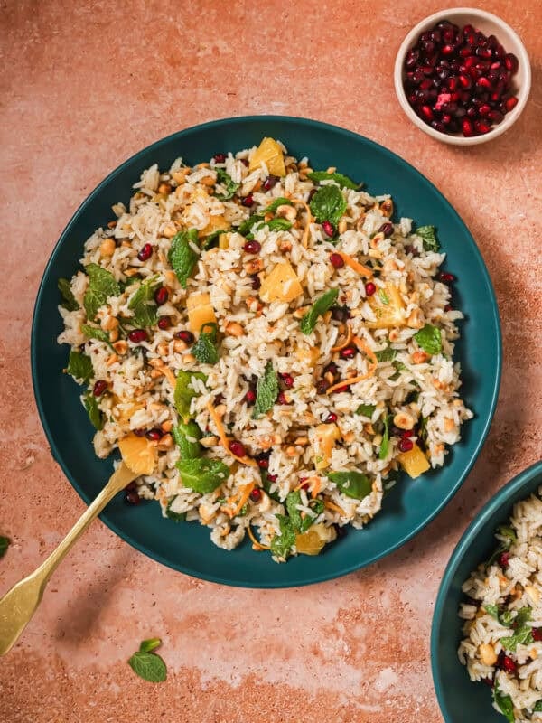 Bowl of herbed rice salad on a table next to a small bowl of pomegranate seeds.