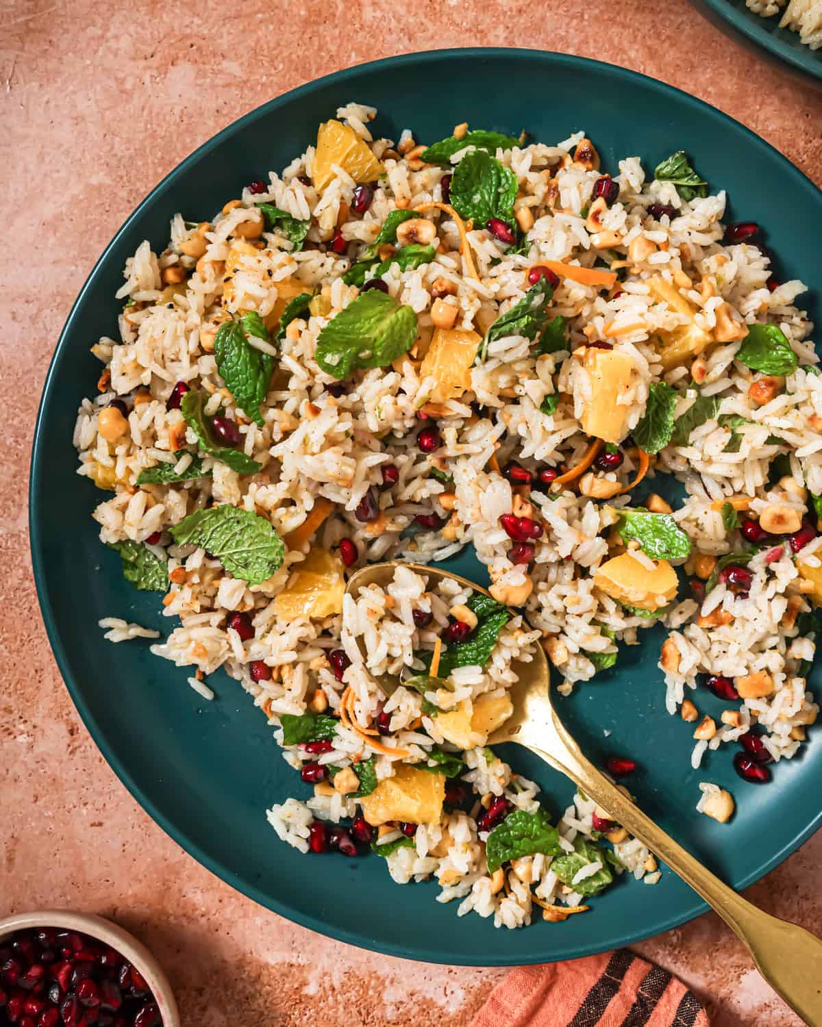 Bowl of herbed rice salad on a table next to a small bowl of pomegranate seeds.