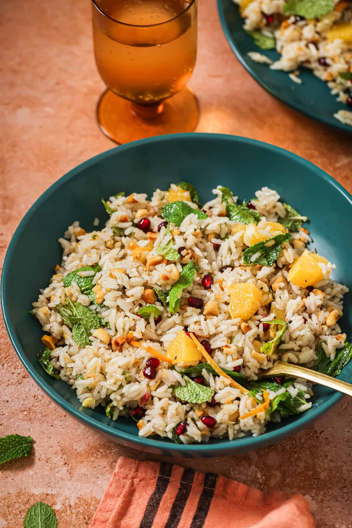 spoon in a bowl of herbed rice next to a filled glass on the table.