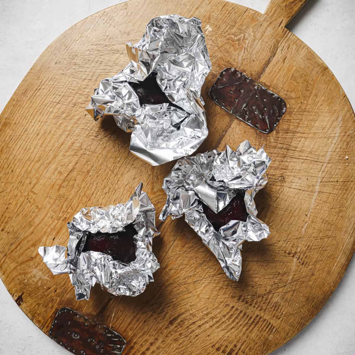 raw beets wrapped in aluminum foil on a wooden cutting board.